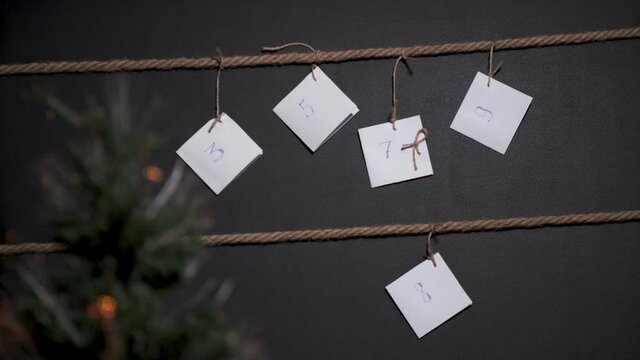 homemade DIY advent calendar, created on a black background and tied with a craft string, in the foreground is a Christmas tree with a garland