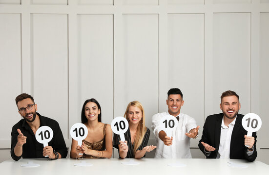 Panel of judges holding signs with highest score at table against light wall