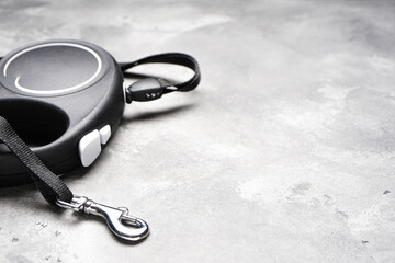 Black retractable dog leash on a gray background, space for text, close-up.