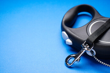 Black retractable dog leash on a blue background, space for text, close-up.