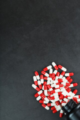 Pills with drugs are scattered from a black jar on a black background.