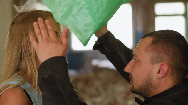 Bearded man takes off plastic bag from young blonde woman hostage head saved from criminals in old ruined building close side view slow motion