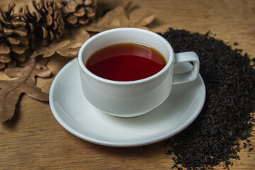 A cup of tea next to black loose tea. Cup of strong black tea on wooden background