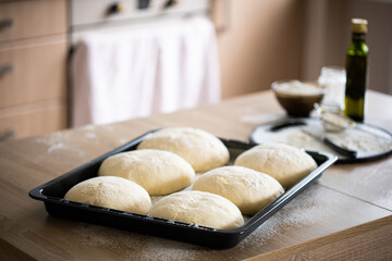 Pre-baked loaves of bread dusted with flour on baking sheet on table with other ingredients in kitchen