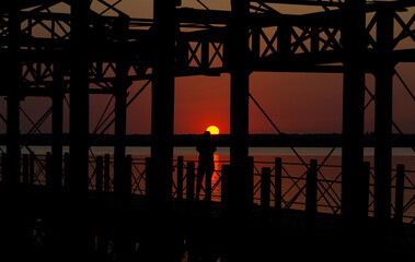 sunset with very orange backlight, totally black human figure and metallic structure in the port of huelva