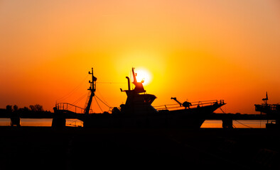 boat in the port of huelva with sunset falling into the sea with a totally orange backlight