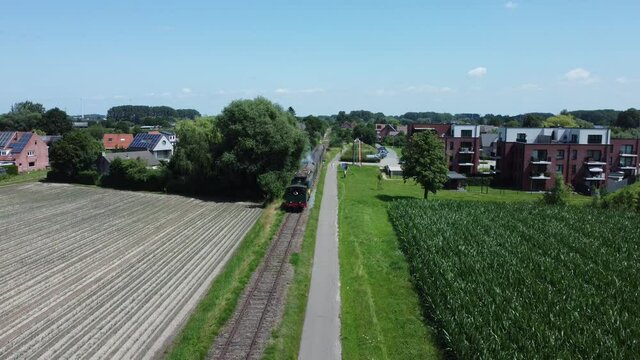 Steam train on rail tracks riding towards the drone. Front view of train while the train driver can be seen. Train riding in fields in Dendermonde, Belgium. Aerial drone shot.