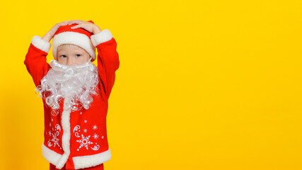 Child in New Year's Santa Claus costume and white fake beard grabbed his head, copy space, yellow isolated background.