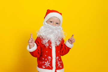 Three-year-old Caucasian child in Christmas Santa Claus costume and white fake beard showing index finger pointing up.