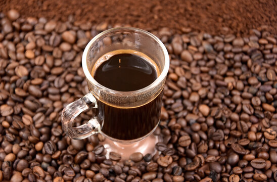 Cup of black hot coffee with roasted coffee beans stock images. Coffee in a small glass cup and pile of roasted coffee beans stock photo