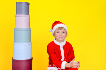 Happy smiling caucasian child sitting near a tower of round gift boxes, yellow background.