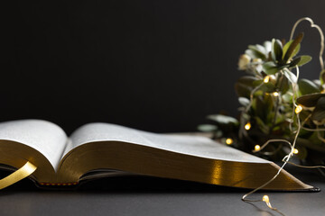 open bible with border of green branches and christmas lights on a black background with copy space