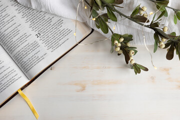 Open bible with Christmas sprig with white berries with lights on a white wood background with copy space