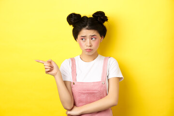 Upset frowning teenage girl sulking, pointing fingers left with jealous unfair face, standing...