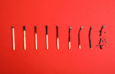 Different stages of burnt matches on red background, flat lay