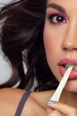 Half beautiful close-up portrait of a girl with long curly hair and evening pink makeup. The girl pulls the gum out of her mouth. Extremely long eyelashes and gentle facial skin care