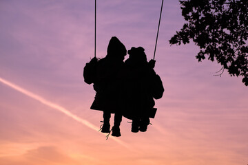 silhouettes of friends of children swinging on a beautiful sunset on a swing