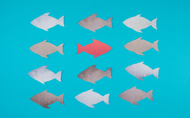 One red fish is swimming against the stream, opposite direction of the other fishes, being different, leadership and mindset concept 