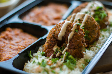 Falafel with sauce over white rice and sprinkled with parsley meal to-go. 