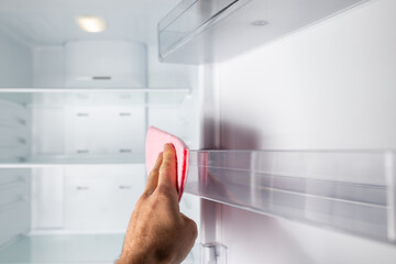 Refrigerator cleaning and maintenance services. Hand cleaning fridge with piece of cloth. - obrazy, fototapety, plakaty