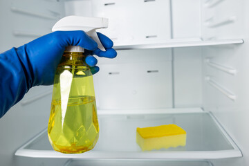 Detergent spray for cleaning refrigerator. Hands in gloves cleaning fridge.