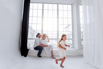 Fototapeta premium Happy family is having fun while sitting on the windowsill by the panoramic window. Woman pregnant