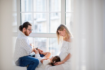 Obraz premium Little girl laughs lies on the lap of pregnant mother the father tickles daughter. Happy family