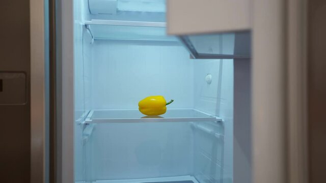 Hungry man is looking for food in fridge at night. Only pepper is inside empty fridge. World job economy crisis and financial crash concept.