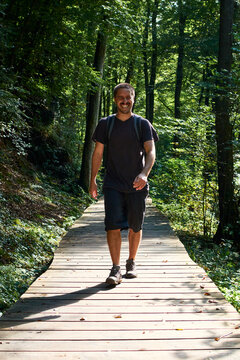 A Hispanic Man With A Backpack Walking On A Wooden Path In The Forest