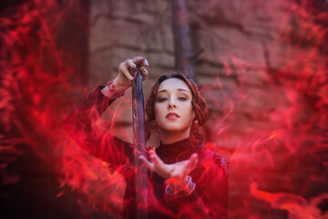 Evil witch with a staff in the forest. Slavic witch creates red magic. A young woman in a black...