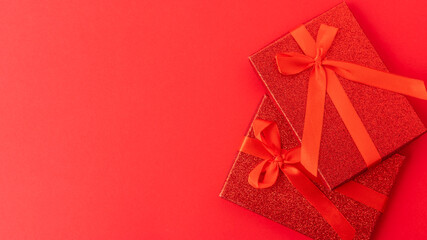 Beautiful stylish composition - gifts in red festive packaging, tied with a red gift ribbon on a red background. Empty space for an inscription. Birthday, Christmas, Valentine's Day. Congratulation.