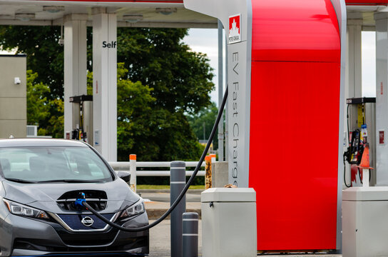 September 5, 2021; Brockville, Ontario, Canada. Daylight front view of a car being charged at a public fast charging station next to a self-serve gasoline pump.