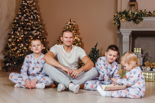 Man And Three Children In Pajamas Sitting On The Carpet Near The Christmas Tree