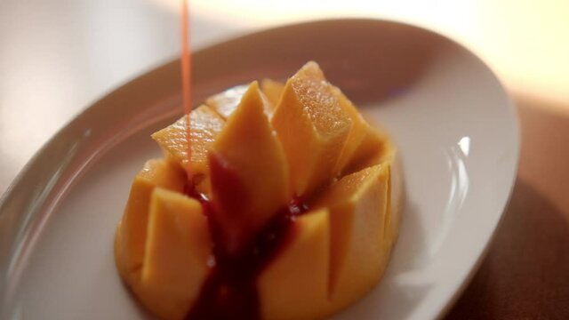 Pouring Mexican chamoy onto chopped mango on white plate