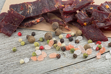 Dried peppered beef jerky pieces with peppercorns and sea salt on wooden background