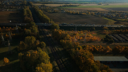 Flight over the railway line. An overpass across the railway is visible. There is a lot of transport on the highway. Yellowed autumn leaves on the trees. Aerial photography.