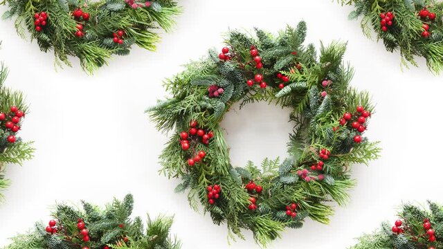 Slow motion of seamless pattern with Christmas wreath of natural evergreen branches, holly berry on white background. Xmas traditional decorations. 4k video.