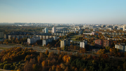 Fototapeta premium Flight over the autumn park. Trees with yellow autumn leaves are visible. On the horizon there is a blue sky and city houses. Aerial photography.