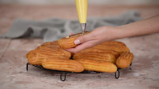 The pastry chef fills the eclairs with creams from a pastry bag.