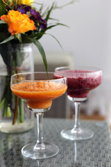 Healthy and delicious colorful homemade smoothies served in fancy drink glasses with some flowers in the background.