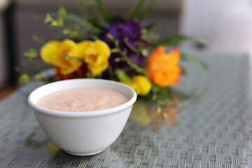 Healthy and delicious colorful homemade smoothie bowl served in a white bowl with colorful flowers in the background.