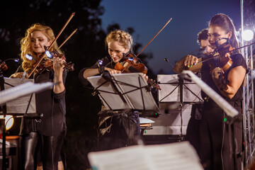Female violin players playing in orchestra at night