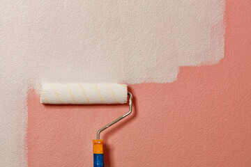 Paint roller paints pink wallpaper on the wall with white paint, copy space.
