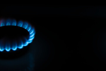 Side view of burning gas stove with blue flame in dark kitchen. Black background. Copy space for your text. Selective focus. Biogas or natural gas. Fuel industry theme.