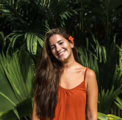 beautiful Hispanic woman smiles in a terracotta dress with a flower on her ear - happiness concept