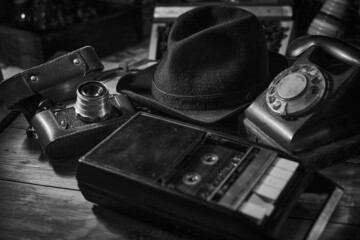 Old vintage cinematic noir scene, detective's desk with a hat, telephone, camera, portable cassette recorder, and whisky