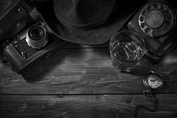 Old vintage cinematic noir scene, detective's desk with a hat, telephone, camera, portable cassette...