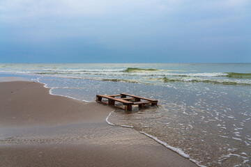 A wooden pallet washes the cold sea against a cloudy sky