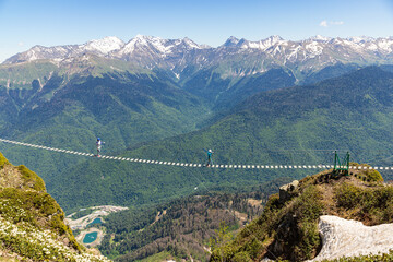 Woman and young boy in a helmets walks on a suspension bridge at Caucasian mountains. Rosa peak, spring. Sochi, Krasnaya polyana.