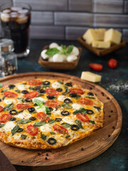 Beautiful composition - a large pizza on a wooden platter and ingredients in the background. Blue background. No people. Italian food. Restaurant, hotel, pizzeria.